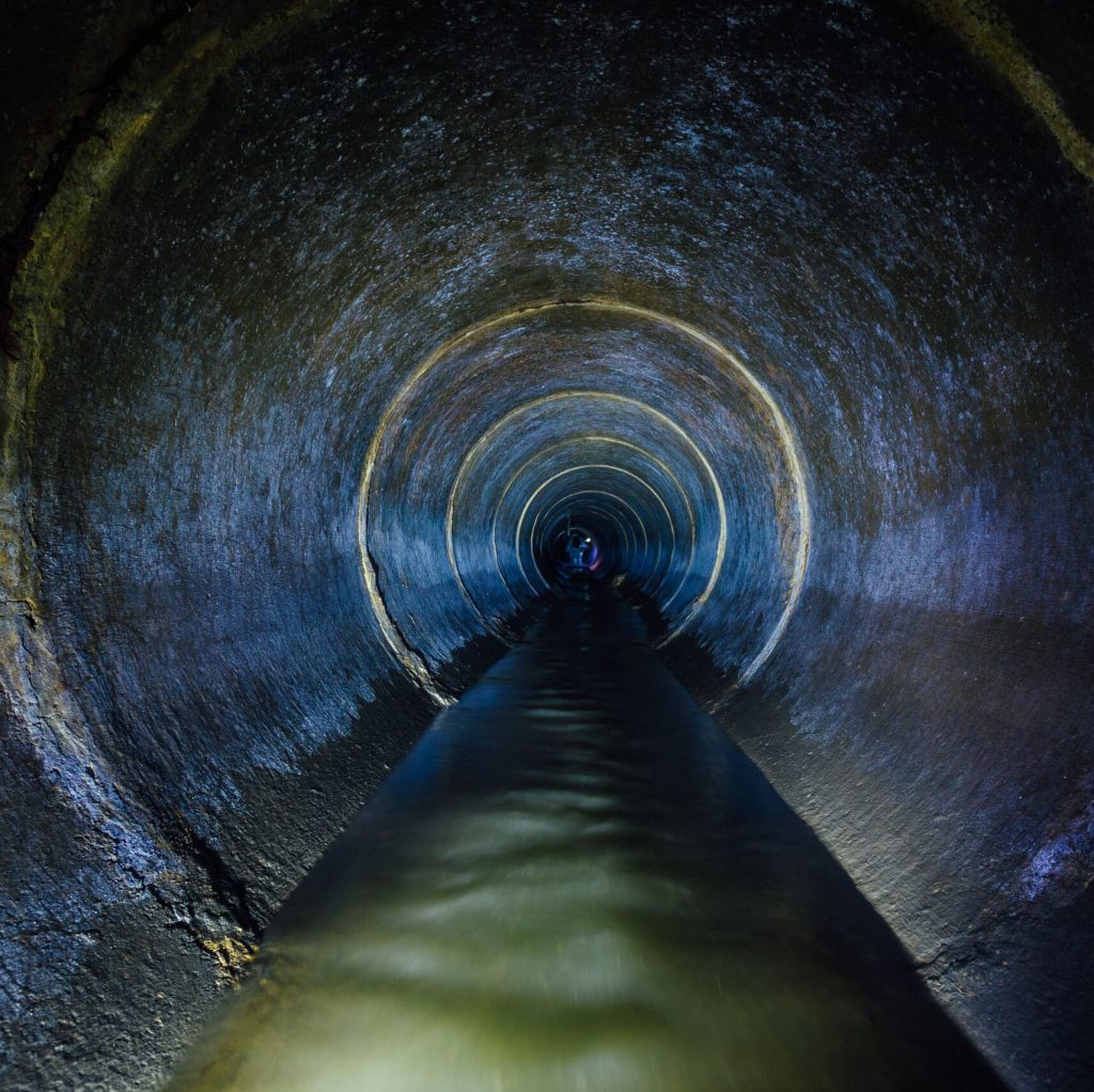 Dark underground sewer round concrete tunnel. Industrial wastewater and urban sewage flowing throw sewer pipe.